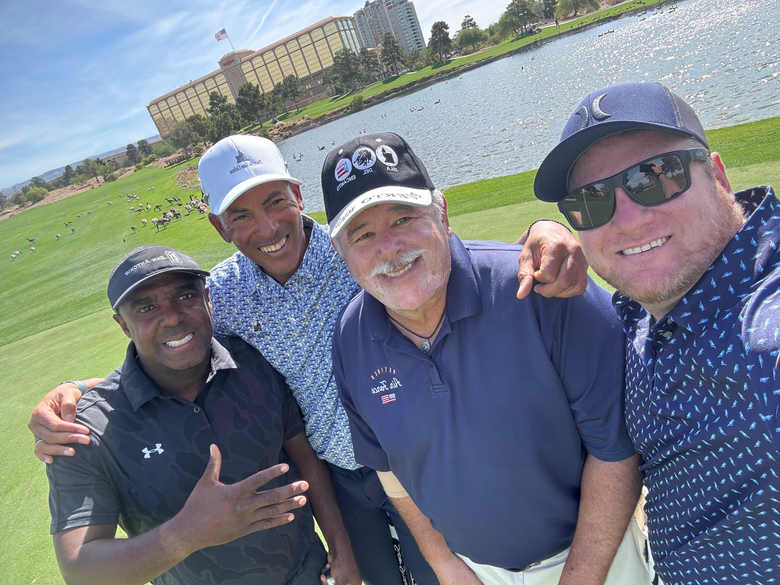 Four Gang Green Golf Club members with their arms around each other beside the water on a course